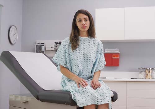 Eine Patientin sitzt auf einer Behandlungsliege  mit Ärztekrepp