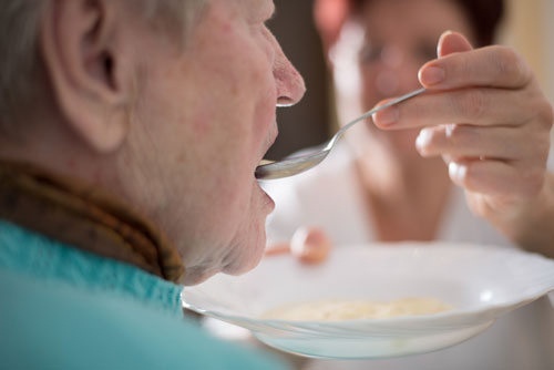 Eine Person wird gefüttert, sie trägt Lätzchen für Erwachsene