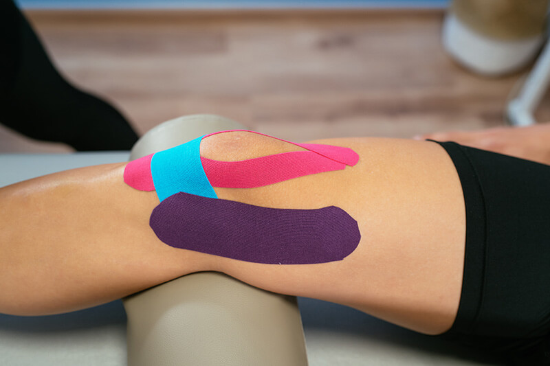 Sporttape wird an das Bein einer Person von einem Therapeuten angebracht