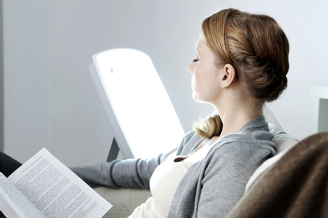 frau liest ein buch während sie sich einer licht therapie unterzieht